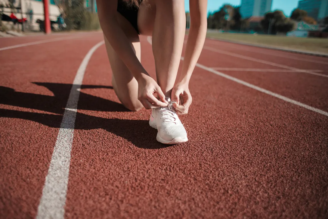 Foto de atleta a atar os cordões das sapatilhas, numa pista de atletismo..